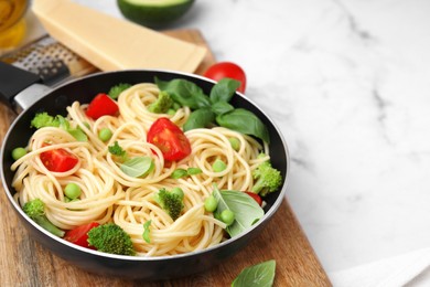 Photo of Delicious pasta primavera in frying pan and ingredients on white table, closeup