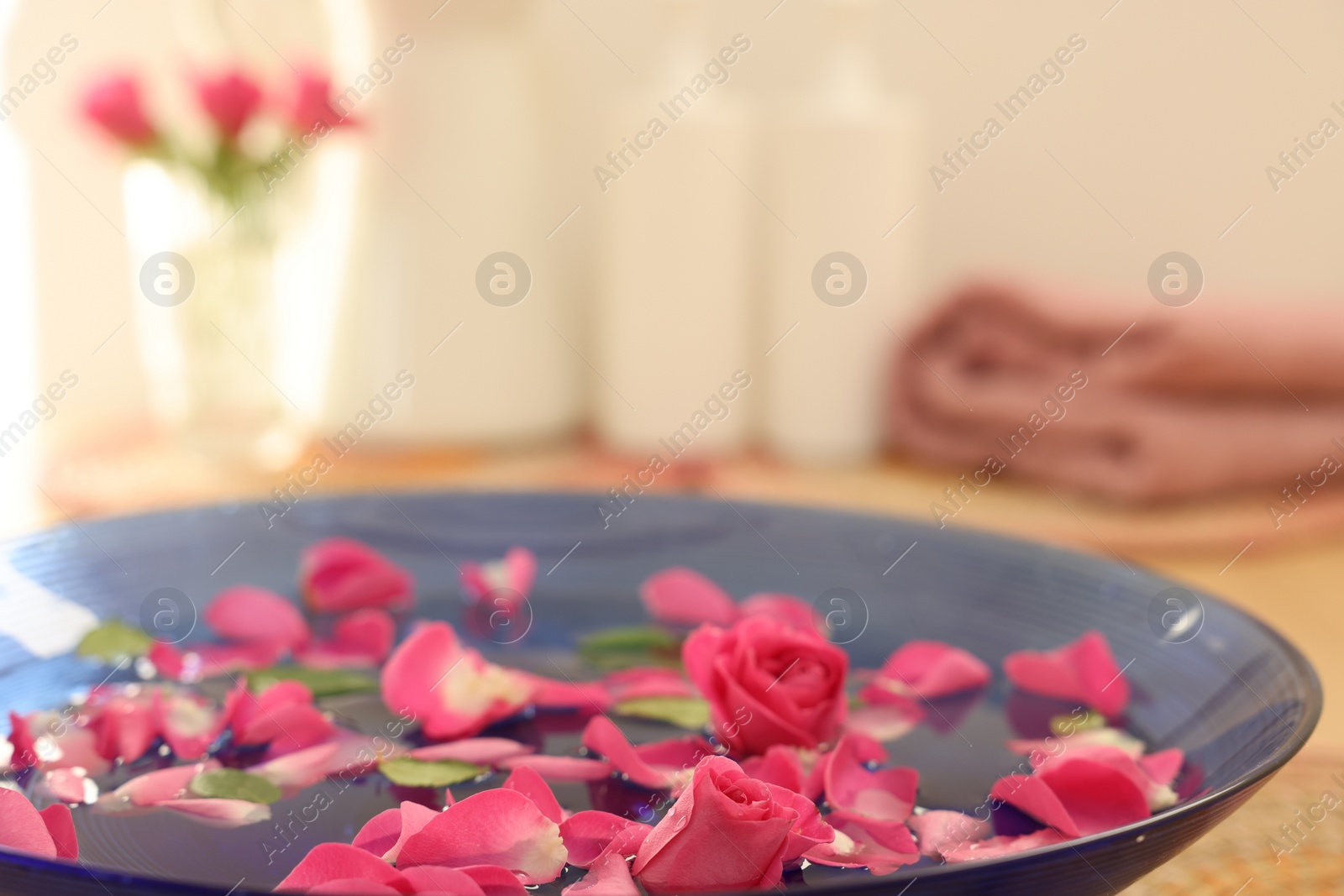 Photo of Pink roses and petals in bowl with water on table, closeup