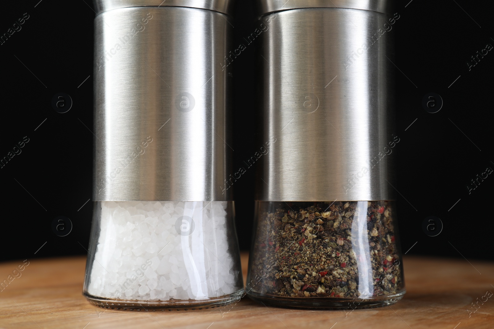 Photo of Salt and pepper shakers on wooden table against black background, closeup