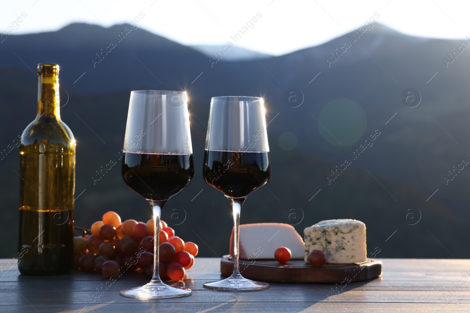 Photo of Red wine served with cheese and grapes on wooden table against mountain landscape