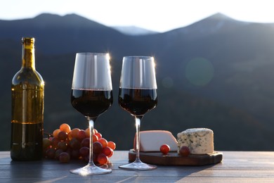 Photo of Red wine served with cheese and grapes on wooden table against mountain landscape
