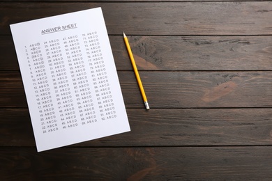 Photo of Answer sheet and pencil on wooden background, top view with space for text