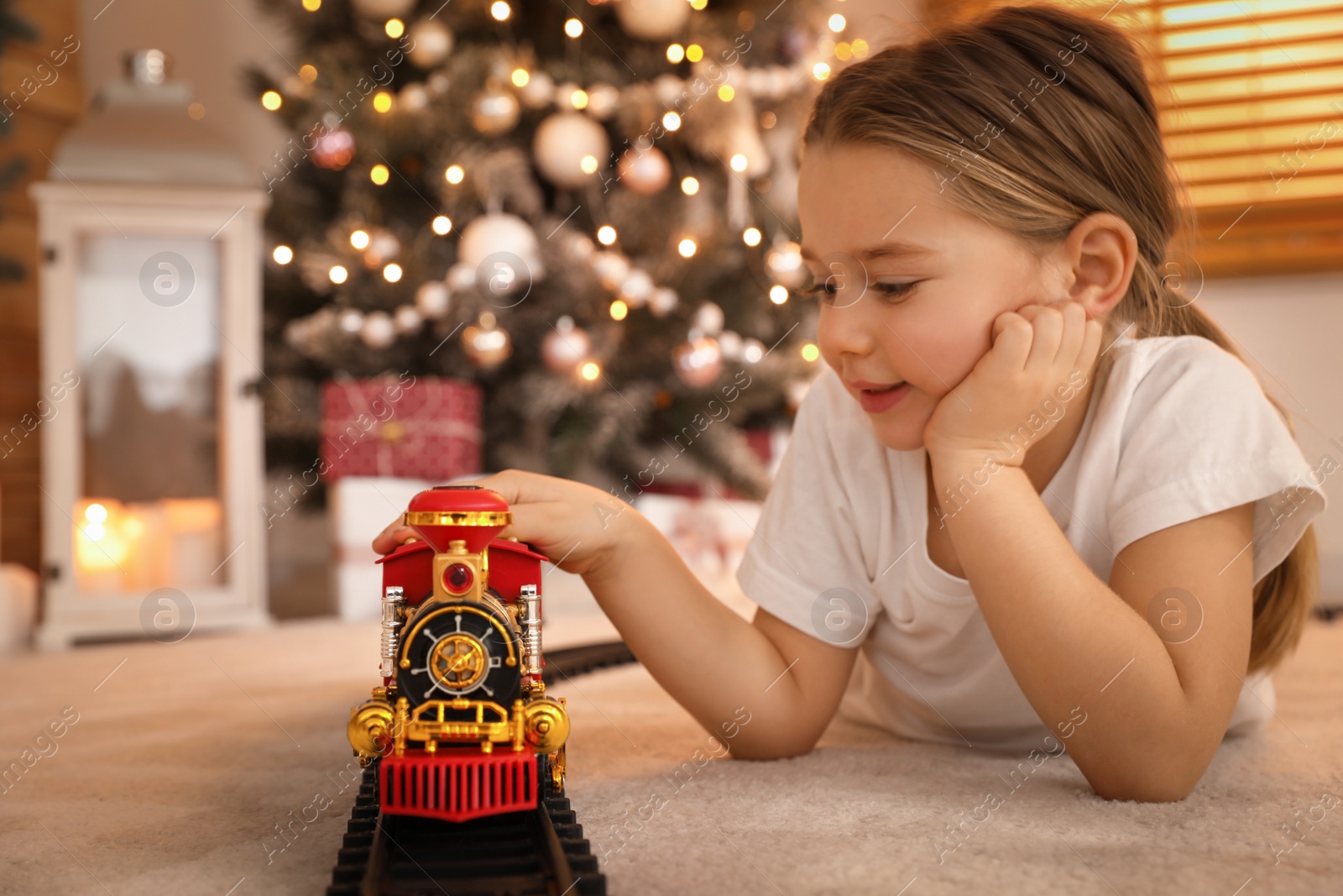 Photo of Little girl playing with colorful train toy in room decorated for Christmas