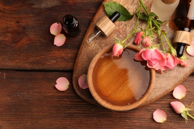 Bowl of essential oil and beautiful roses on wooden table, flat lay with space for text. Aromatherapy treatment