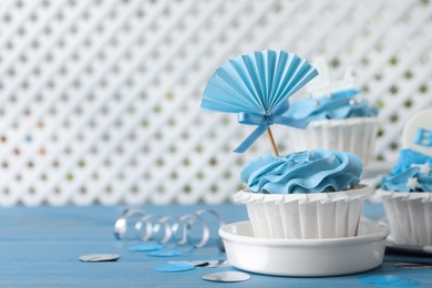 Photo of Delicious cupcakes with light blue cream and toppers on table, space for text. Baby shower party