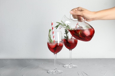 Woman pouring cranberry cocktail into glass with rosemary on table