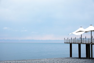 Beautiful view of pier with beach umbrellas near sea. Space for text
