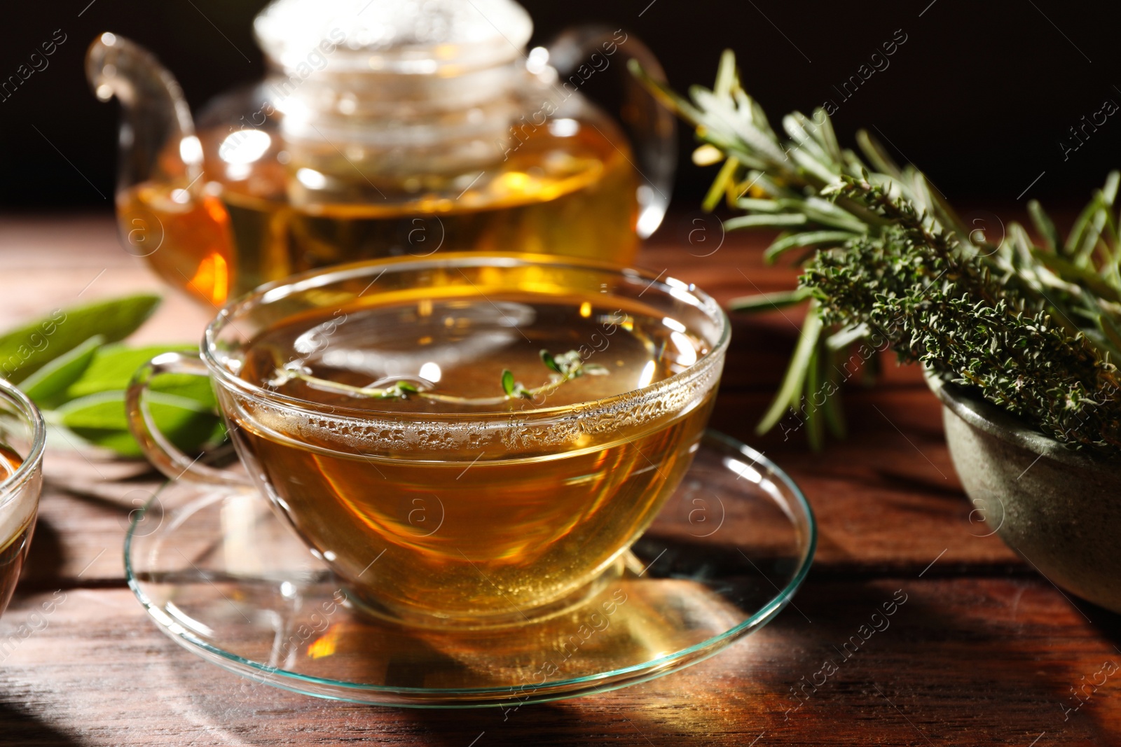 Photo of Cup of aromatic herbal tea, fresh rosemary and thyme on wooden table