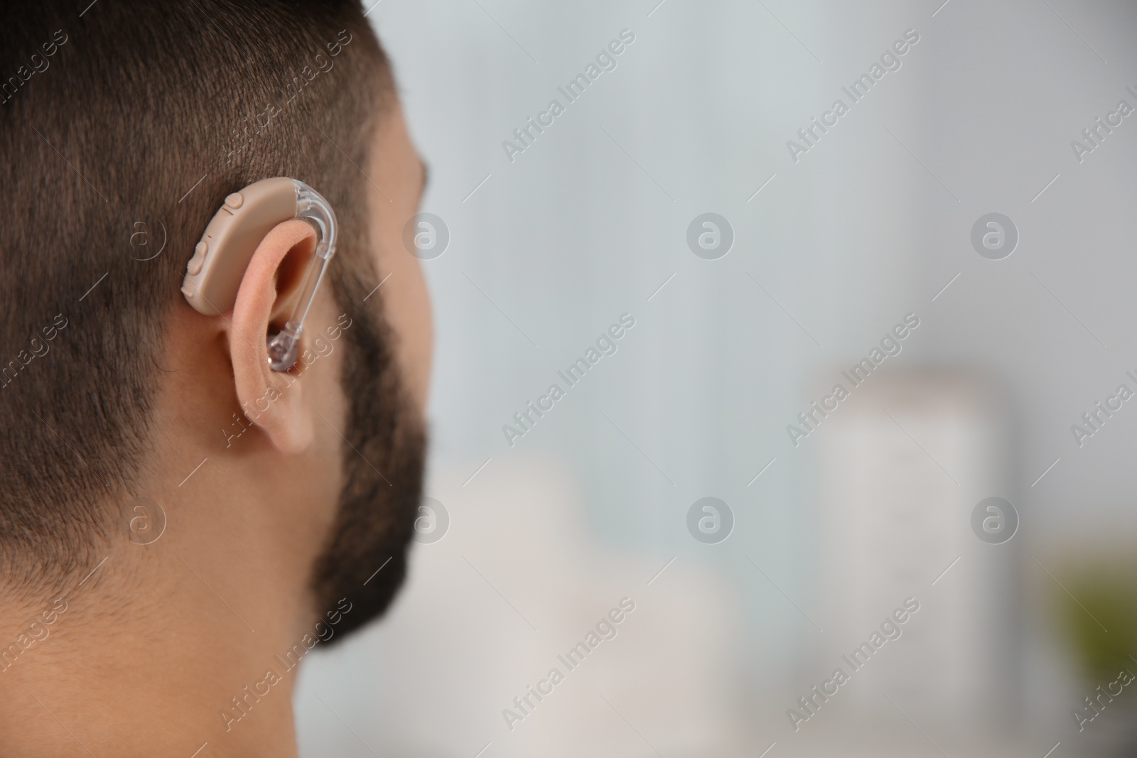 Photo of Young man with hearing aid indoors, closeup. Space for text