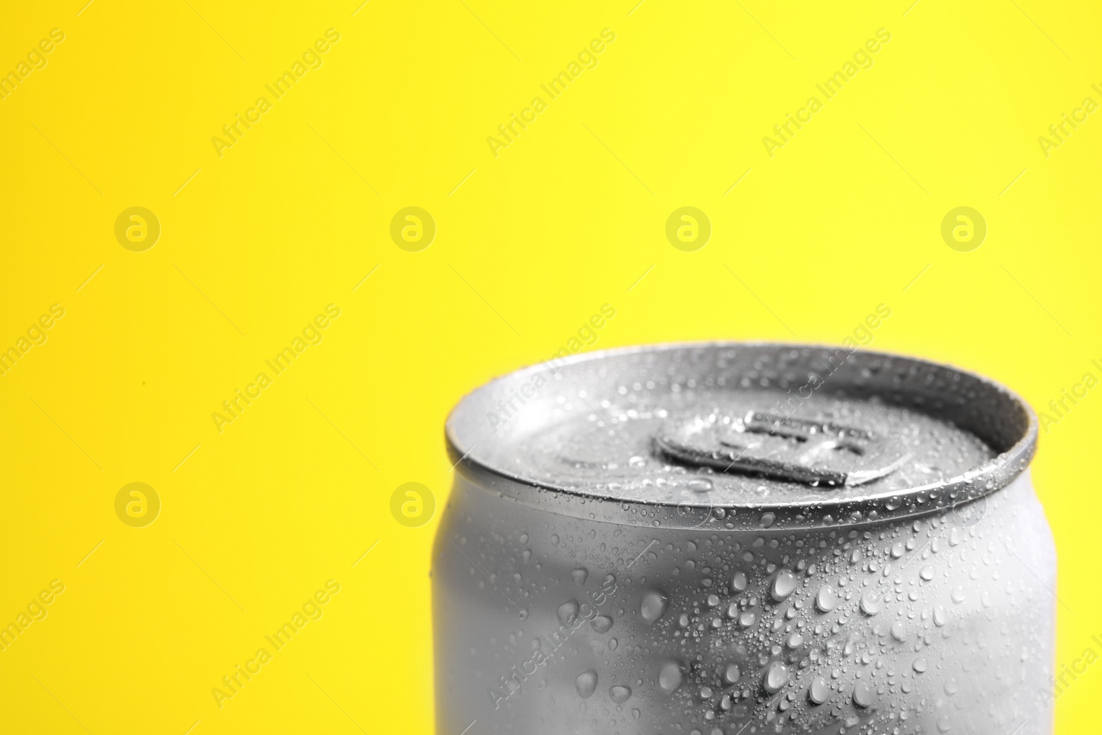 Photo of Aluminum can of beverage covered with water drops on yellow background, closeup. Space for text