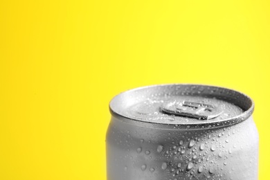 Aluminum can of beverage covered with water drops on yellow background, closeup. Space for text