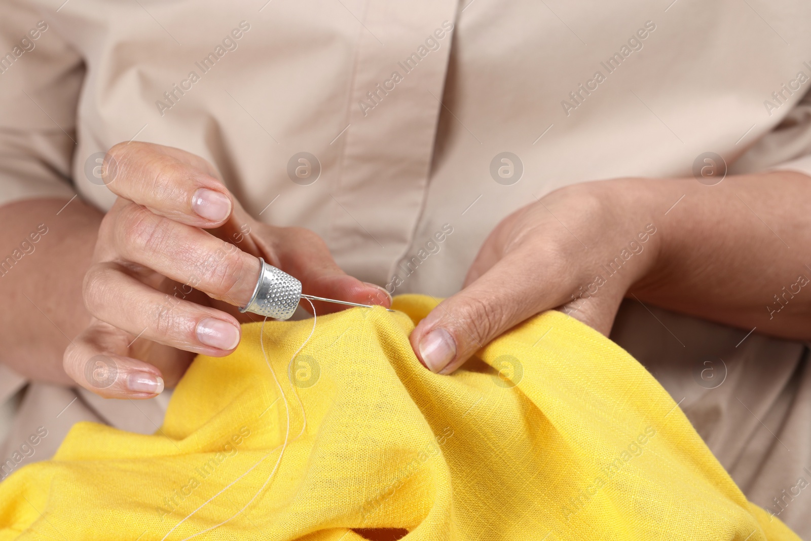 Photo of Woman sewing on yellow fabric with thimble and needle, closeup