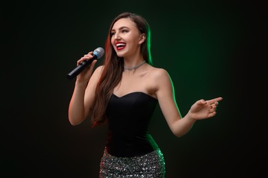 Photo of Emotional woman with microphone singing in color lights on dark background
