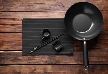 Photo of Empty iron wok, sauce bowl and chopsticks on wooden table, flat lay
