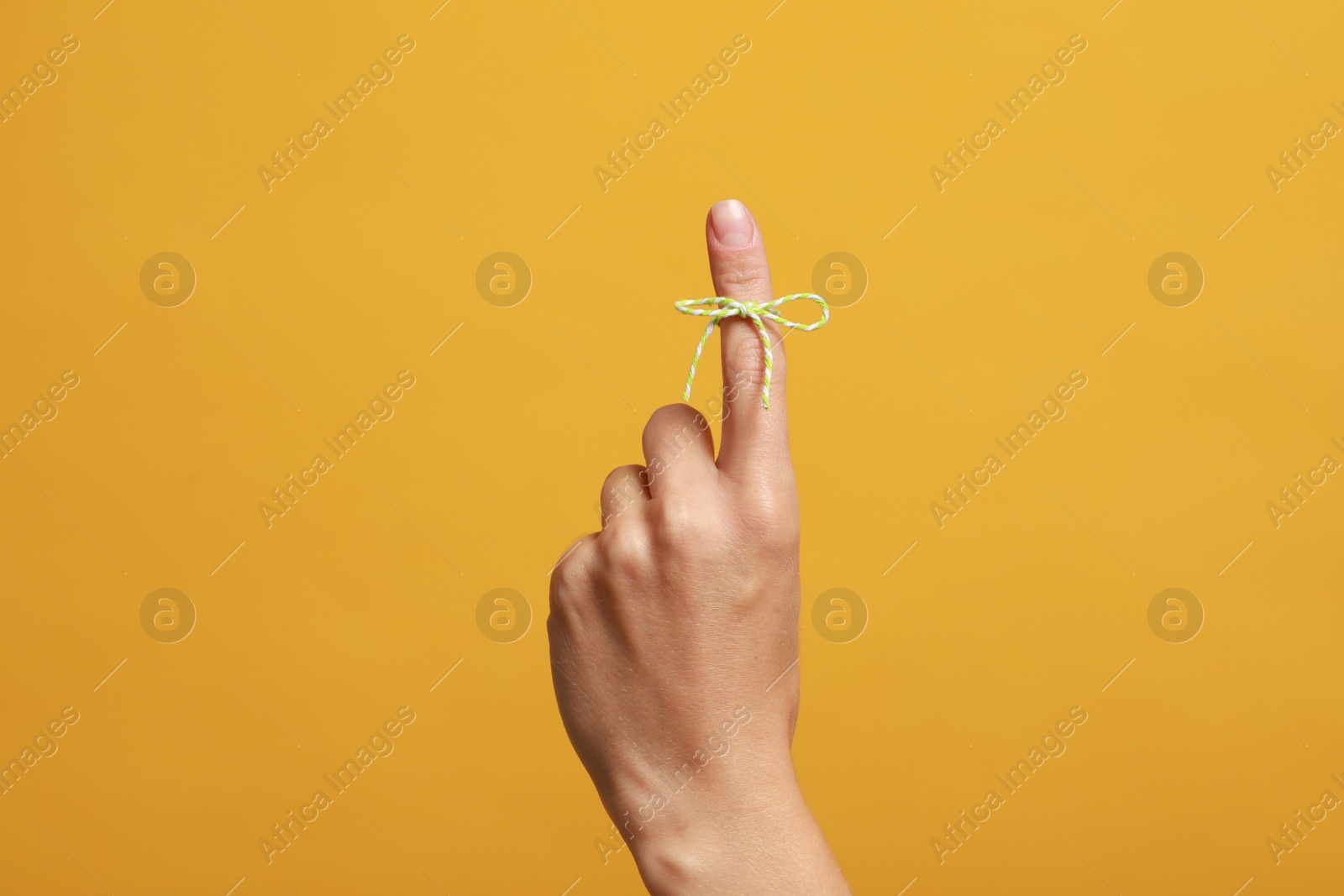 Photo of Woman showing index finger with tied bow as reminder on orange background, closeup