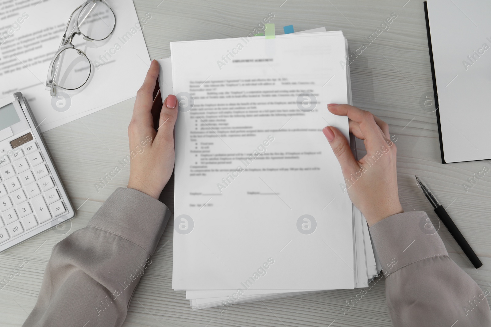 Photo of Woman reading documents, pen and glasses on white wooden table in office, top view