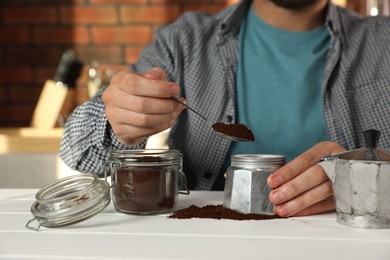 Man putting ground coffee into moka pot at white wooden table indoors, closeup
