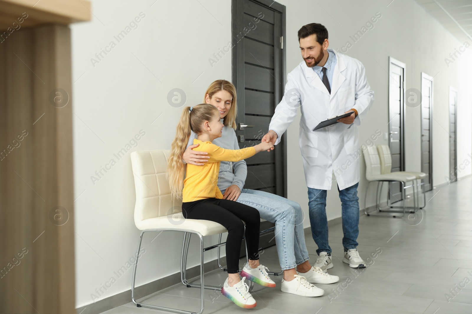 Photo of Mother and daughter having appointment with doctor. Pediatrician shaking hands with patient in clinic