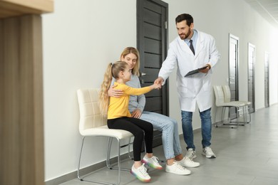 Photo of Mother and daughter having appointment with doctor. Pediatrician shaking hands with patient in clinic