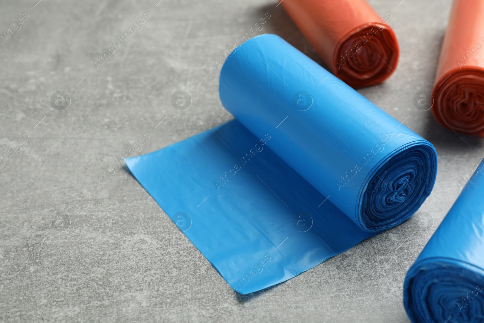 Photo of Rolls of different color garbage bags on light grey stone table