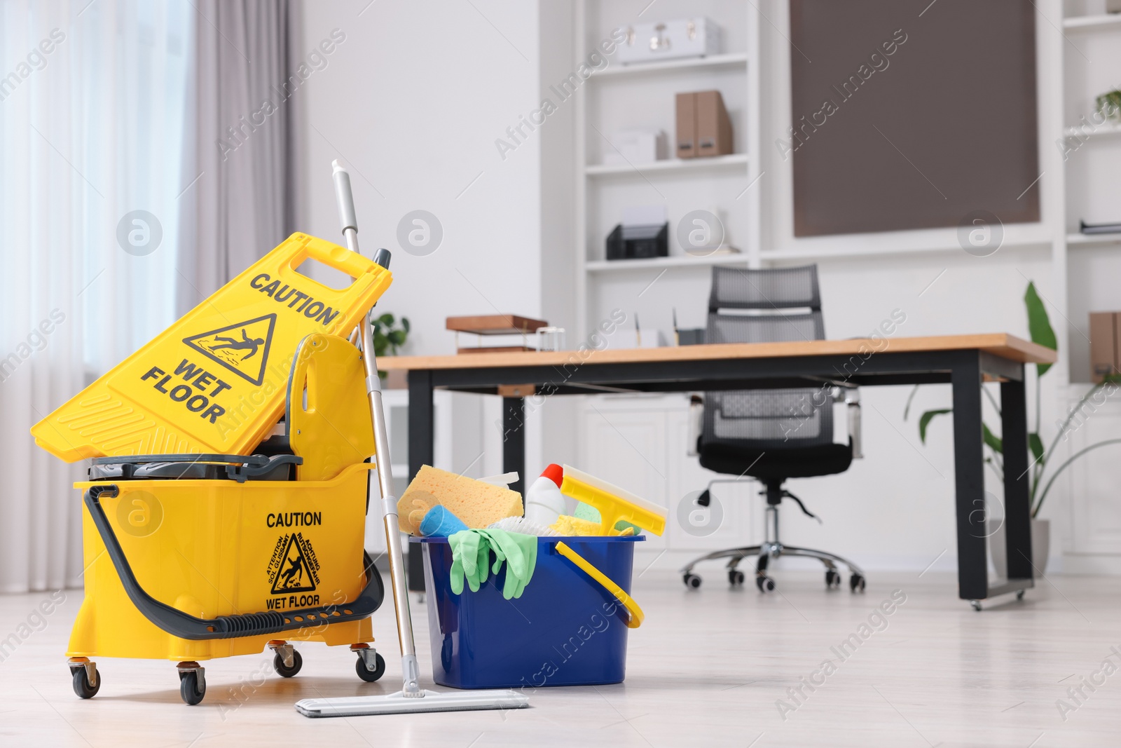 Photo of Cleaning service. Mop, bucket with supplies and wet floor sign in office, space for text