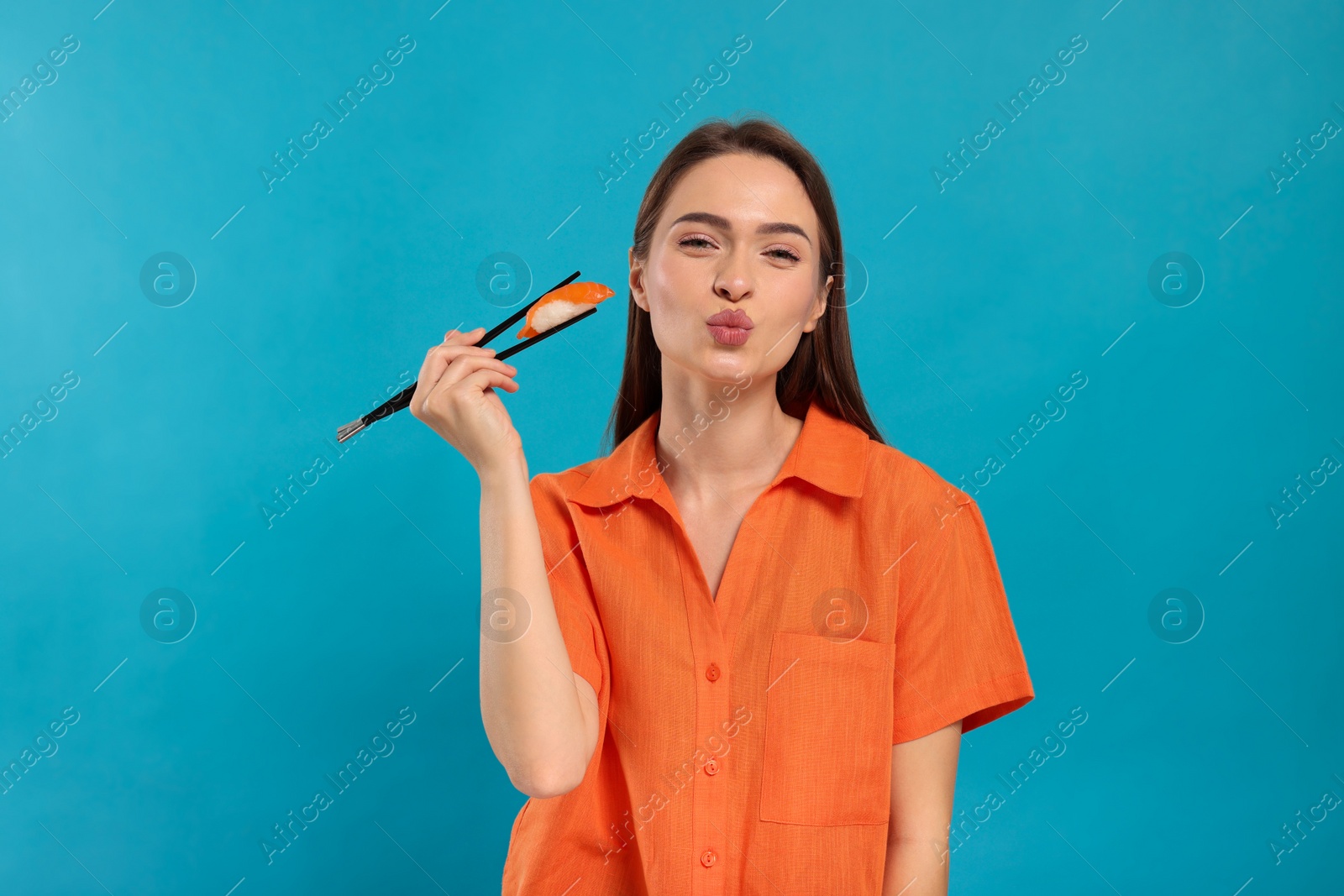 Photo of Funny young woman holding sushi with chopsticks on light blue background