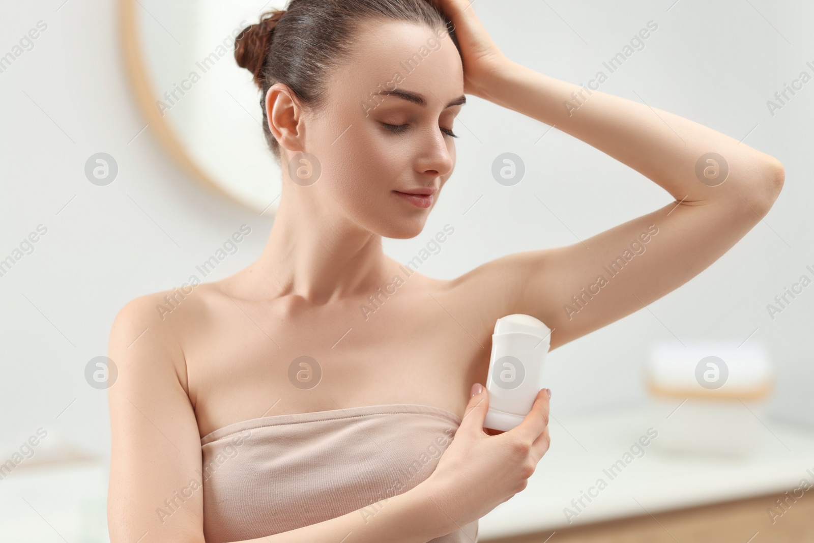 Photo of Beautiful young woman applying deodorant in bathroom