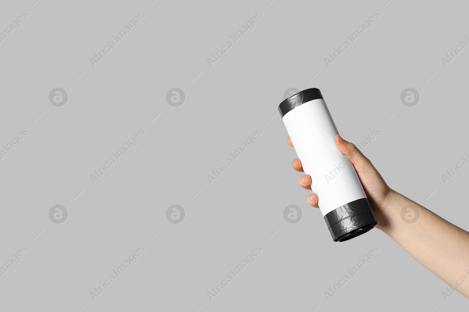 Photo of Woman holding roll of black garbage bags on light grey background, closeup. Space for text