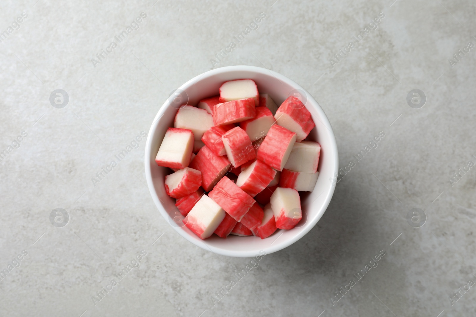 Photo of Cut crab sticks in bowl on light table, top view