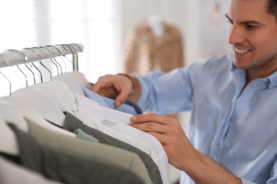 Photo of Man choosing clothes near rack in modern boutique