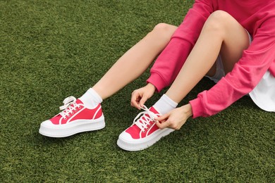 Woman tying shoelace of classic old school sneaker on green grass outdoors, closeup