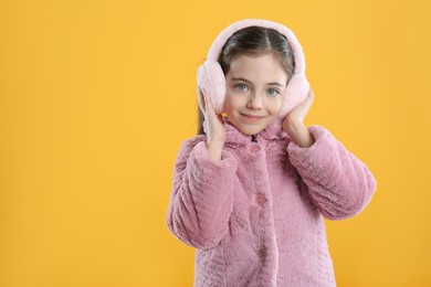 Photo of Cute girl wearing stylish earmuffs on yellow background. Space for text