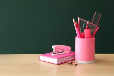 Photo of Different school stationery on wooden table near green chalkboard, space for text. Back to school