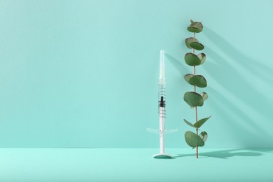 Photo of Cosmetology. Medical syringe and eucalyptus branch on turquoise background, space for text