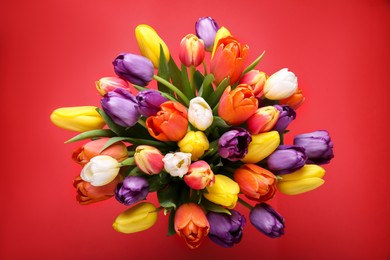 Photo of Bouquet of beautiful colorful tulips on red background, top view