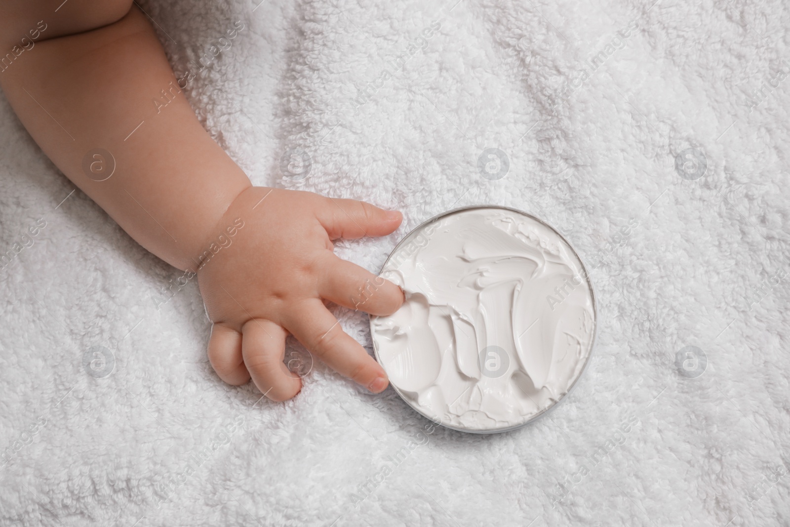 Photo of Cute little baby playing with jar of moisturizing cream on towel, closeup