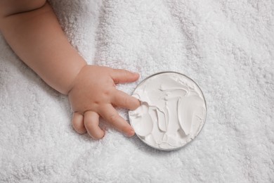 Photo of Cute little baby playing with jar of moisturizing cream on towel, closeup