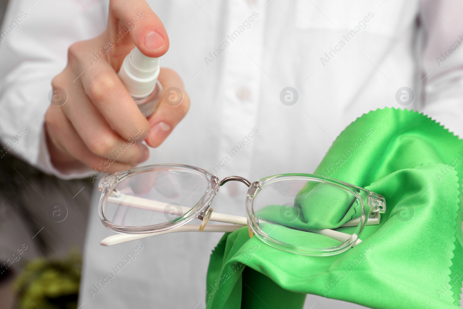 Photo of Woman cleaning glasses with microfiber cloth and spray, closeup