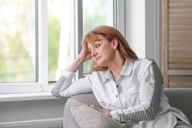 Photo of Senior woman suffering from depression on sofa near window
