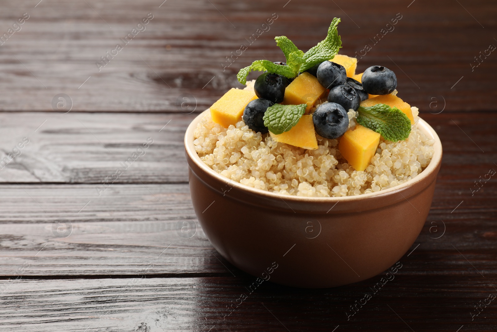 Photo of Tasty quinoa porridge with blueberries, pumpkin and mint in bowl on wooden table, closeup. Space for text