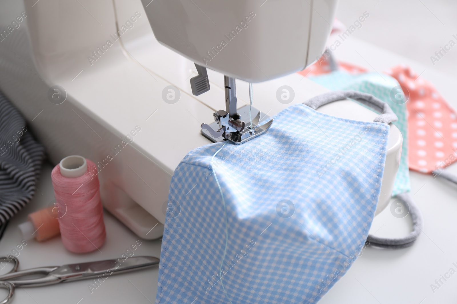 Photo of Sewing machine with cloth mask on white table, closeup