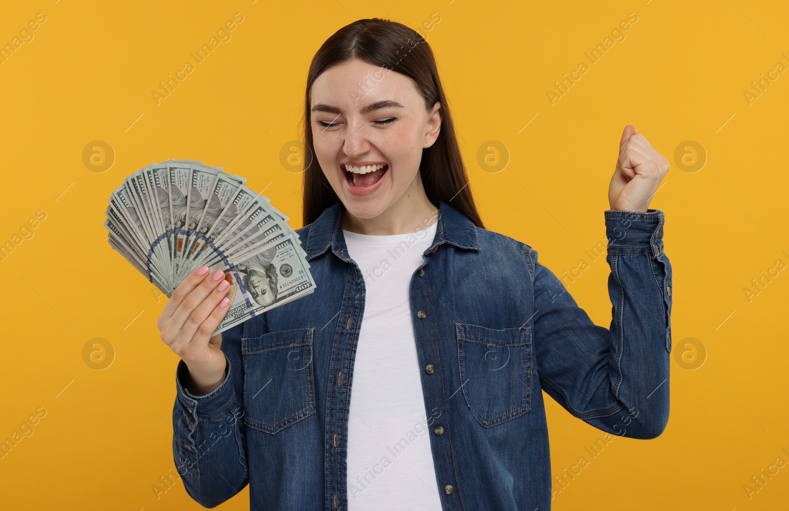 Photo of Excited woman with dollar banknotes on orange background