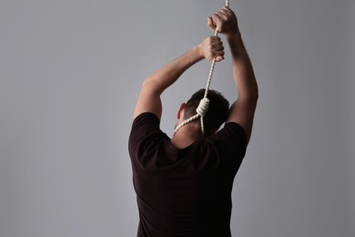 Man with rope noose on neck against light grey background, back view