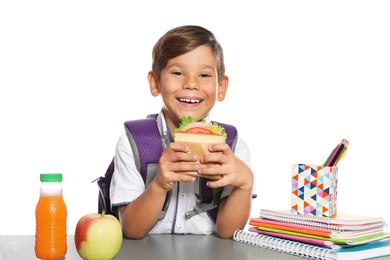 Schoolboy with healthy food and backpack sitting at table on white background