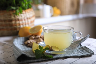 Photo of Glass of aromatic ginger tea and ingredients on white checkered tablecloth indoors