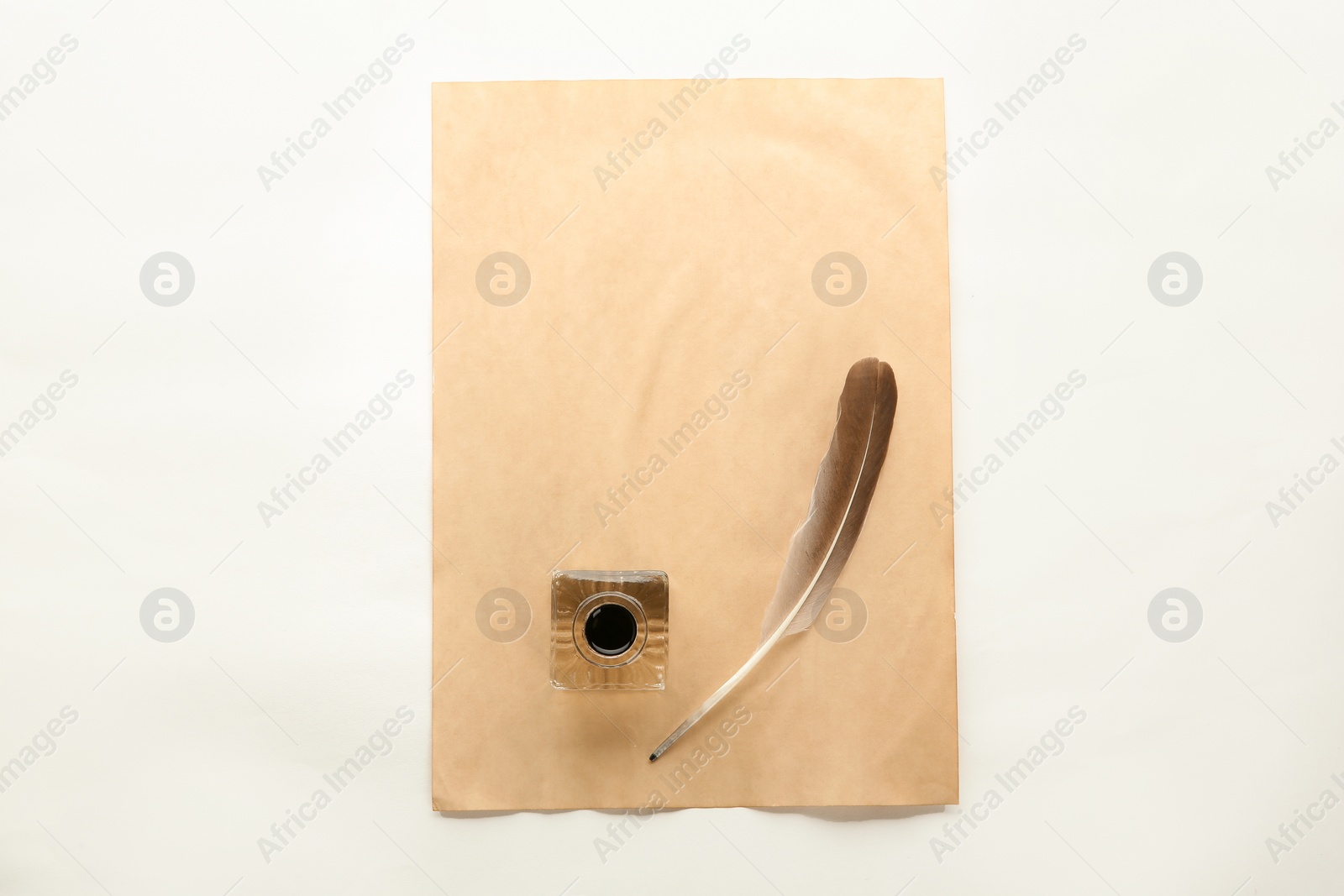 Photo of Feather pen, inkwell and sheet of paper on white background, top view. Space for text
