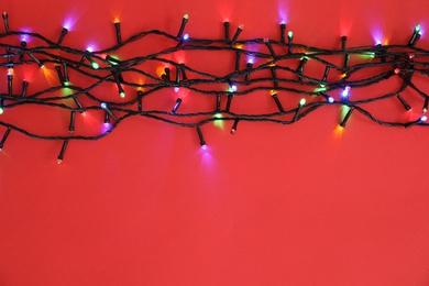 Glowing Christmas lights on color background, top view