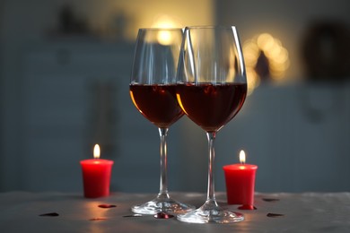 Photo of Glasses of red wine and burning candles on grey table against blurred lights, space for text. Romantic atmosphere