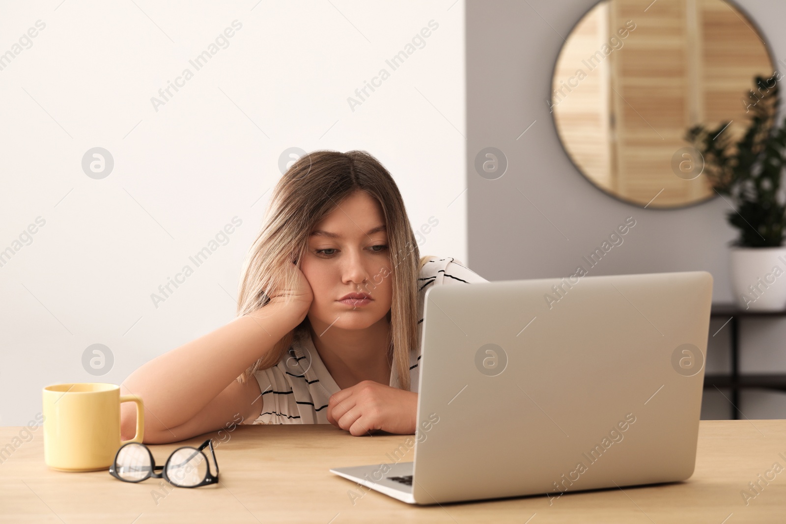 Photo of Sleepy young woman with laptop at wooden table indoors