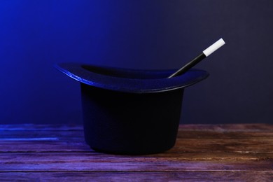 Photo of Black top hat and wand on wooden table. Magician equipment